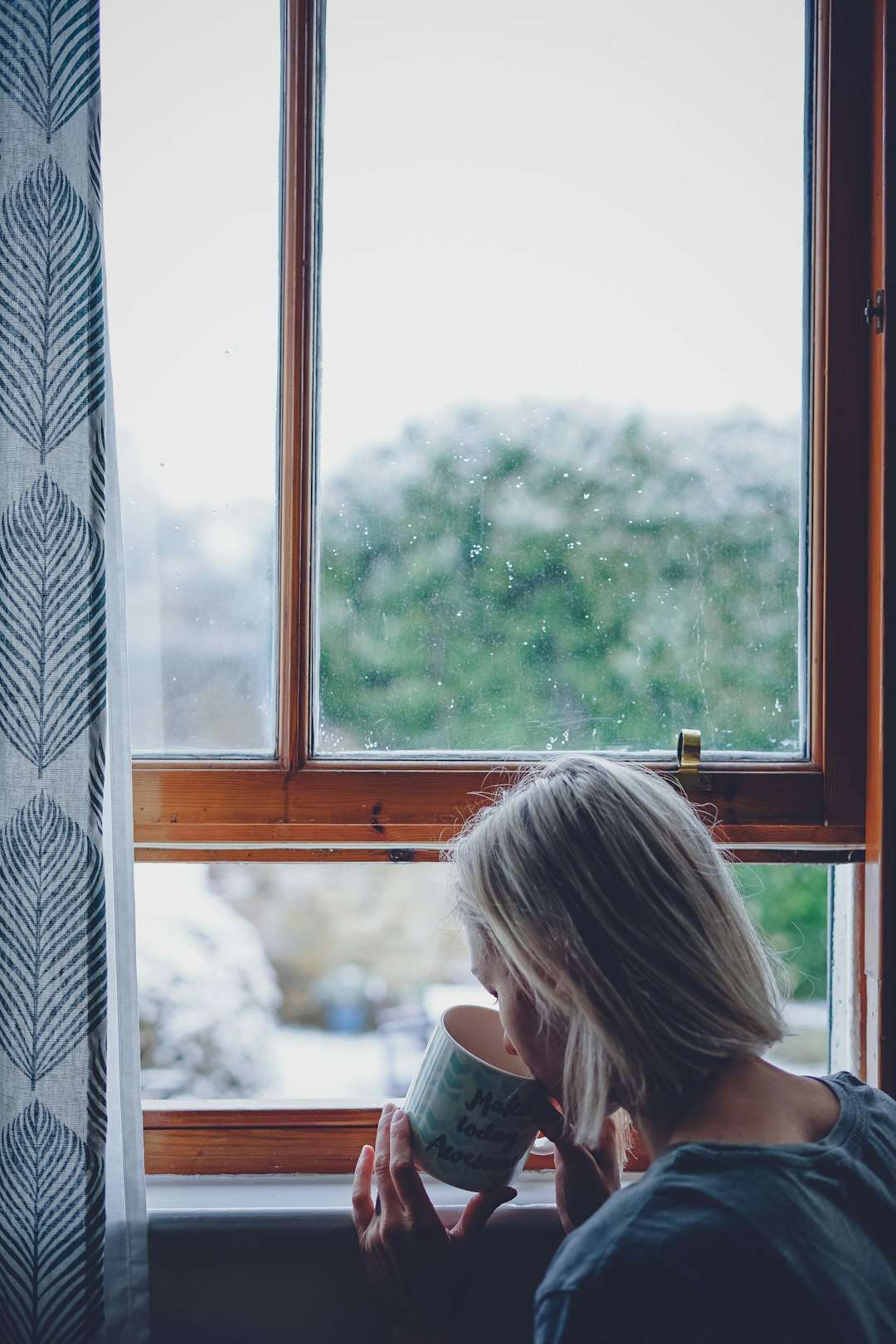 Donna alla finestra che beve una tazza di caffè per tirarsi su