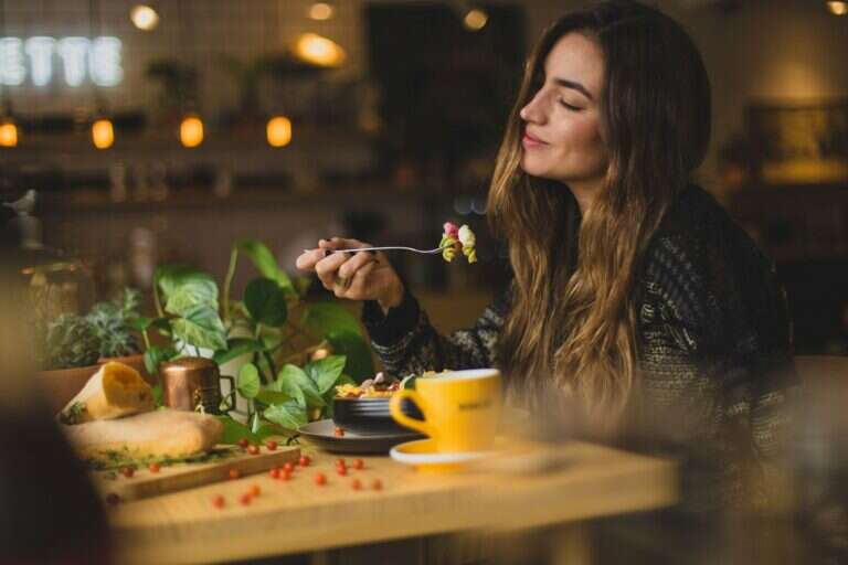 Una donna a tavola con la forchetta in mano: mangiare con attenzione