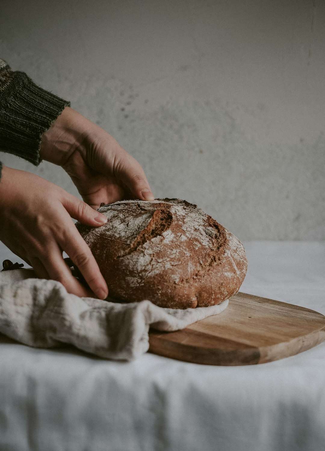 Mani che appoggiano una pagnotta di pane rustico sul tagliere